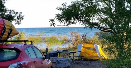 View of waterfront campsite with car, picnic table, and small tent