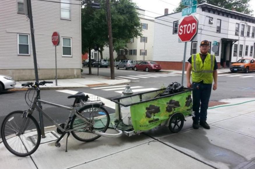 a bicycle with a trailer used for watering with a city worker standing next to it